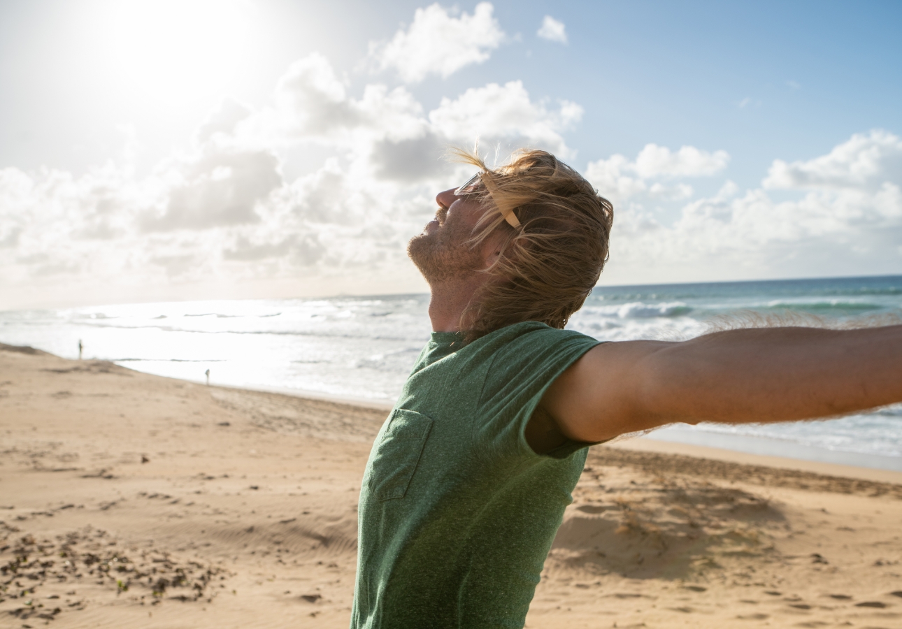A man on a beach with outstretched arms enjoying the sun and the breeze