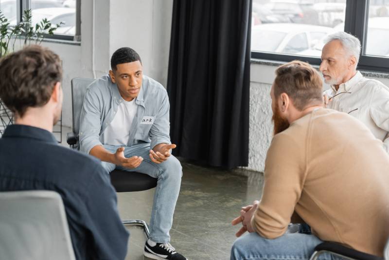 An addiction treatment group therapy session with a young man speaking to the group intently
