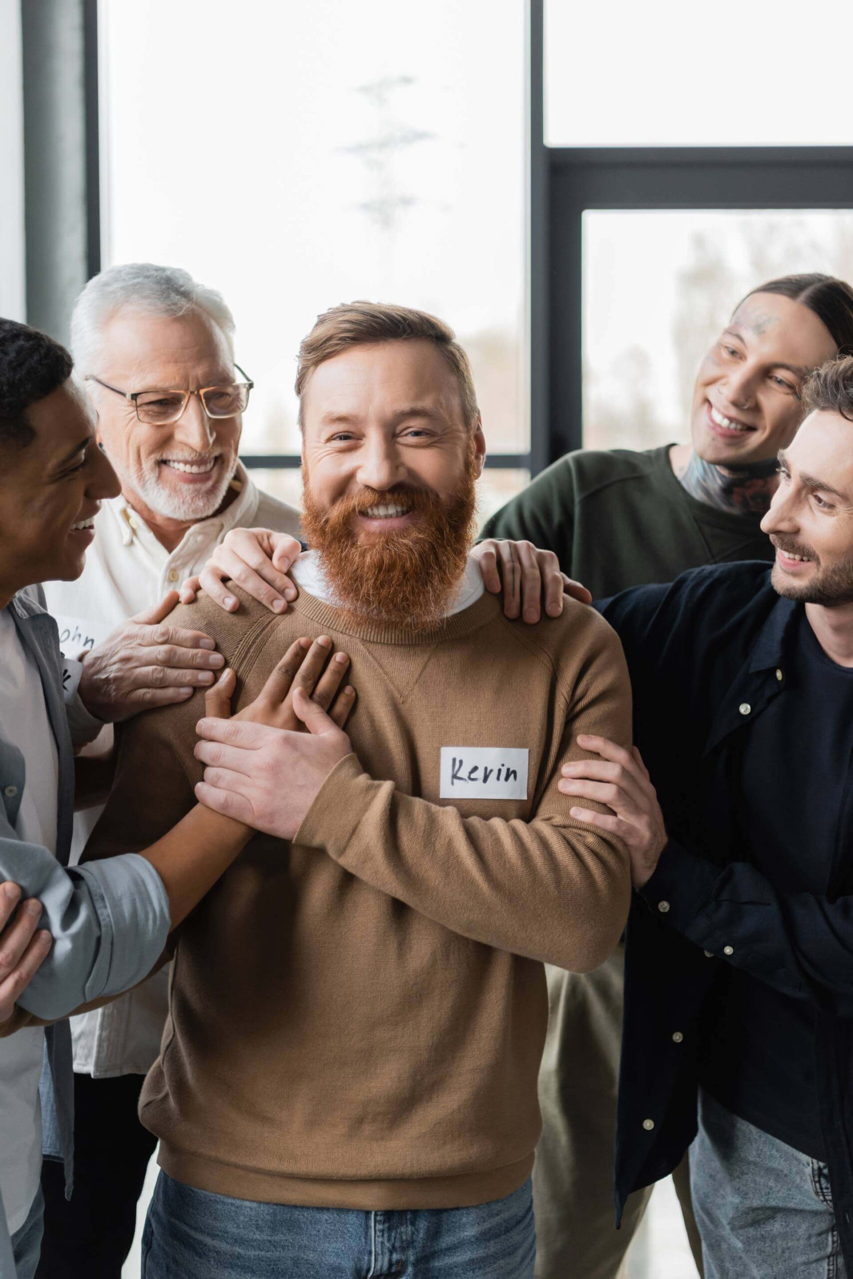 People gathering around a man all smiling and touching his shoulder because they are happy for him.