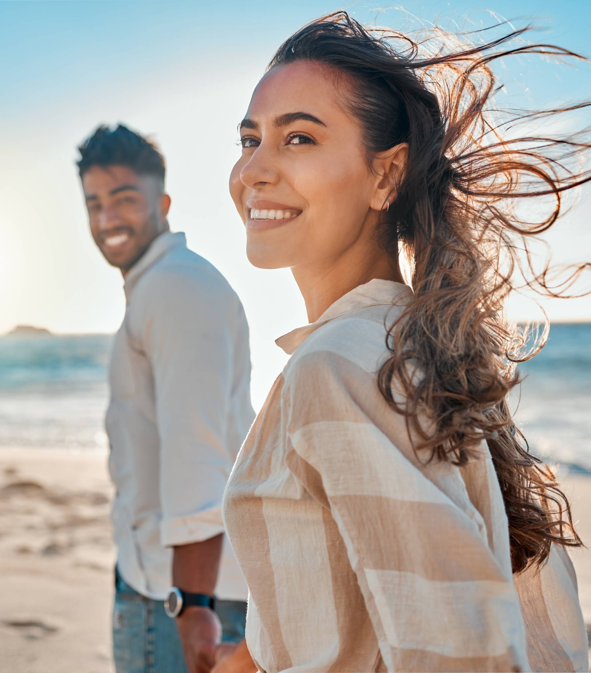 A woman smiling holding hands with a man in the background on a beach