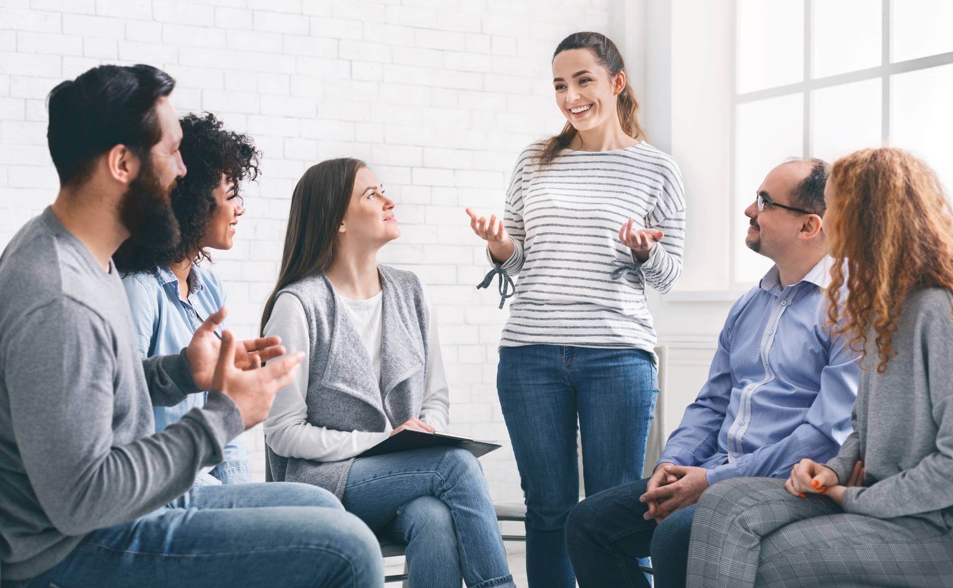 A female addiction treatment patient speaking to a group and smiling