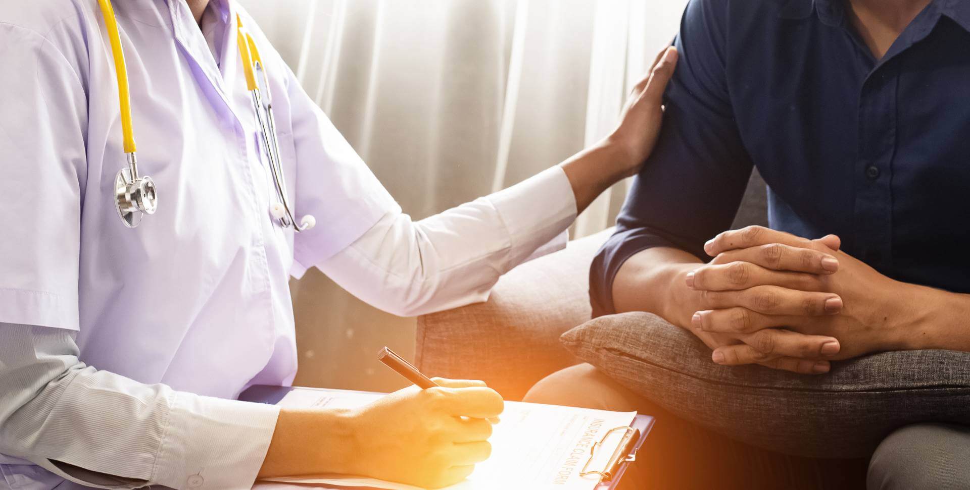 A doctor writes on a clipboard and touches the patient shoulder in a caring way